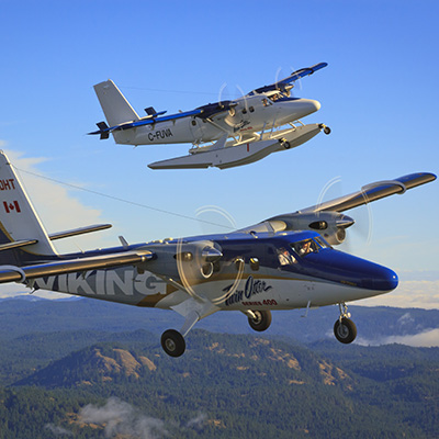 Two Twin Otter aircraft flying over trees and mountains