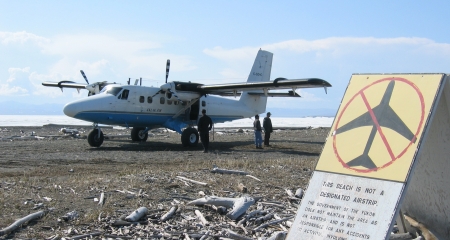 Twin Otter on beach behind a warning sign 