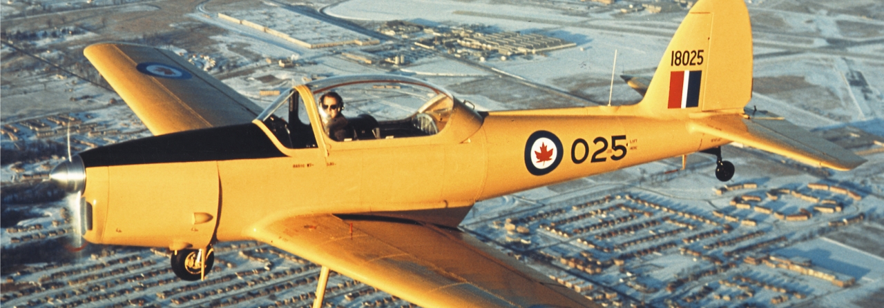 A yellow DHC-1 Chipmunk flying over a city